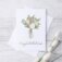 Congratulations card staged on white distressed wood background. Card features watercolor bouquet with "congratulations" written in calligraphy