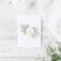 "Oh Baby" greeting card staged on distressed white wood background with eucalyptus leaves and white chiffon at the corner. Artwork features a watercolor floral wreath with "oh baby" in calligraphy