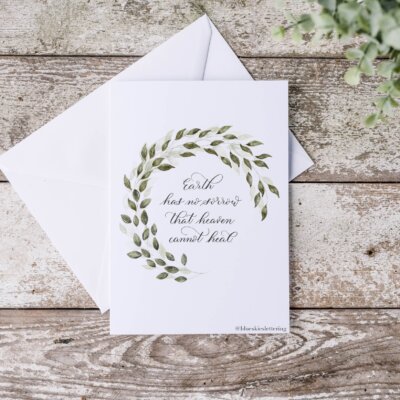 Sympathy-Cards Sympathy card message staged on distressed wood background with eucalyptus. Artwork features semi-circle leaf wreath with "earth has no sorrows that heaven cannot heal" Thomas Moore in calligraphy